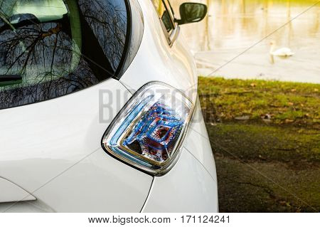 Rear view of an supermini electric city car parked in front of ecologiacl lake with swans having fun on a cold summer day