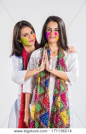two Indian beautiful girl in namaskar pose or welcoming with hands folded on holi festival, with coloured face, in indian traditional wear and dupatta, isolated over white background with copyspace