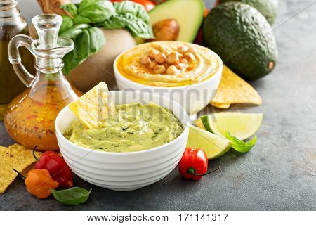 Guacamole and hummus in white bowls with vegetables and corn chips