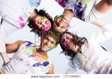 young Indian happy friends or couples with heads together in circle celebrating holi festival, with faces coloured with gulal