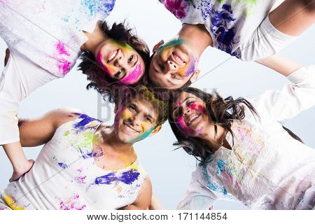 young Indian happy friends or couples with heads together in circle celebrating holi festival, with faces coloured with gulal