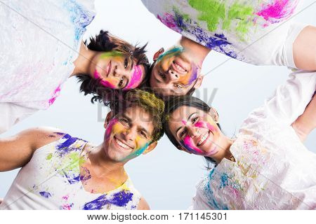 young Indian happy friends or couples with heads together in circle celebrating holi festival, with faces coloured with gulal