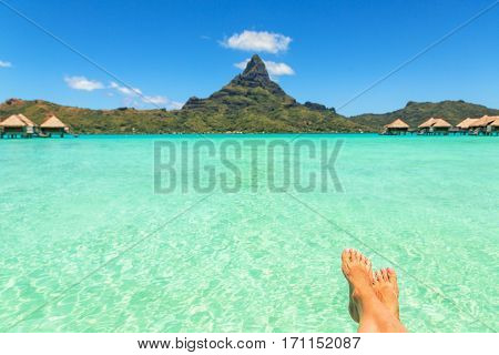 Female crossed legs over tropical blue lagoon and Otemanu mount Bora Bora near Tahiti in French Polynesia.