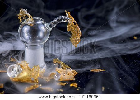Close up detail of marijuana oil concentrate aka shatter isolated on black background with glass rig and smoke