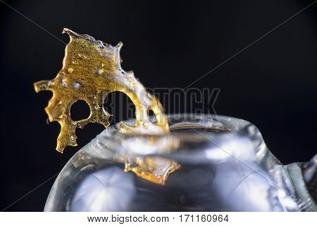 Close up detail of marijuana oil concentrate aka shatter isolated on black background with glass rig and smoke