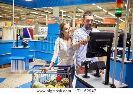 shopping, sale, payment, consumerism and people concept - happy couple with credit card buying food at grocery store or supermarket self-service cash register