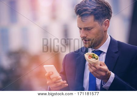 Handsome businessman using mobile phone while holding snacks