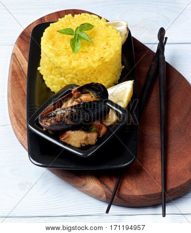 Arrangement of Delicious Seafood Curry with Mussels White Fish and Vegetables and Stack of Saffron Rice with Chopsticks on Serving Board closeup on Wooden background