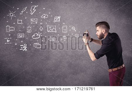 An elegant hipster guy trying to use a vintage camera with camera settings icons drawn on wall, like flash, white balace or ISO value concept