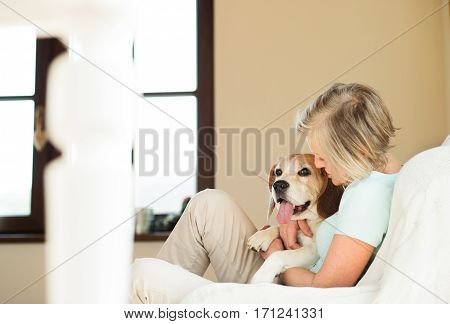 Beautiful senior woman with her dog at home sitting on couch, relaxing