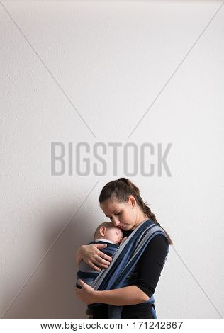 Beautiful young mother with her baby son sleeping in sling. Studio shot on white background. Copy space.