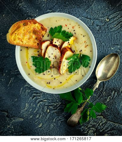 Creamy chicken soup with vegetables in bowl with chiabatta toast, parsley and nigela seeds sprinkle on stone table.