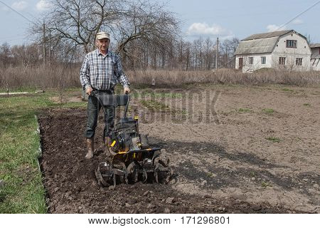 Man working in the garden with garden tiller. Garden tiller to work. Man with tractor cultivating field at spring. Farmer loosens soil by petrol cultivator