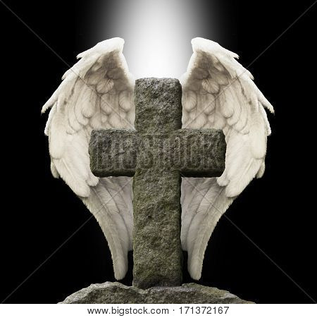 Ancient Stone Cross and Guardian Angel Wings - old masonry cross with a pair of white angel wings behind on a black background with a shaft of central white light