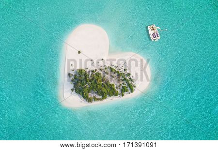Beautiful small tropical island in heart shape, catamaran boat anchoring.