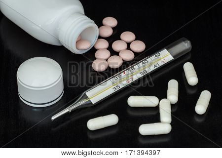 Mercury thermometer white capcules and pink pills with bottle on dark background