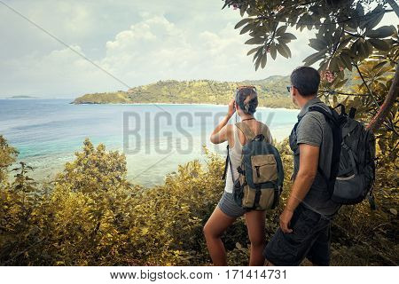 Couple tourists with backpacks enjoying view coast island Lombok on top of a mountain. Traveling along mountains and coast freedom and active lifestyle concept.