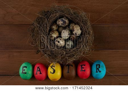Easter holidays tradition and object concept - close up of colored easter eggs and quaill eggs in nest on wooden surface.Top view.