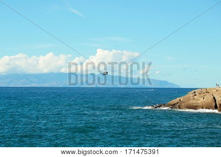 Parachute flies above beautiful blue sea water inshore along rocky coast outdoors on sunny summer day on sky background
