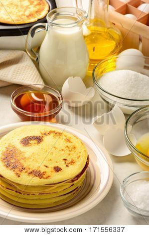 Pancakes and ingredients for making pancakes on a white background