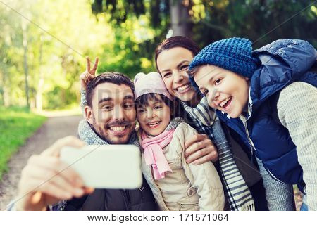 technology, travel, tourism, hike and people concept - happy family with backpacks taking selfie by smartphone and hiking