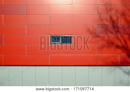 The front facade of a modern building of gray and red panels wih small window. Shadows of the trees on the facade of the building. Architectural background.