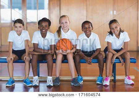 Portrait of school kids sitting in basketball court at school