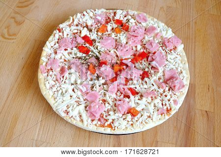 Raw unready pizza on sandy brown wooden kitchen table top view closeup