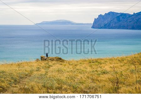 A man stands on a rock and looking at the sea and the mountains