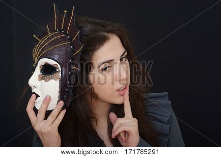 actress brunette holding an old theatrical mask in hands against a dark background