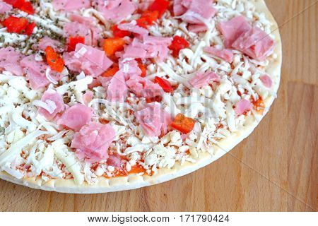 Still life with part of unready pizza on sandy brown wooden kitchen table top view closeup