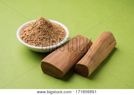 Chandan or sandalwood powder with traditional mortar, sandalwood sticks, perfume or oil and green leaves. selective focus
