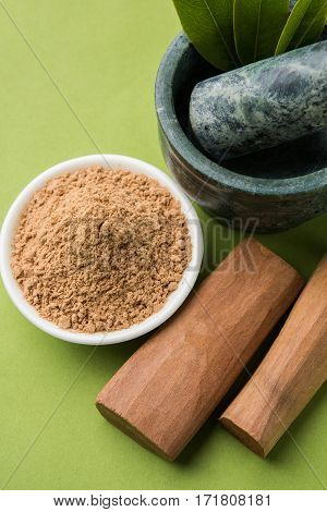 Chandan or sandalwood powder with traditional mortar, sandalwood sticks, perfume or oil and green leaves. selective focus