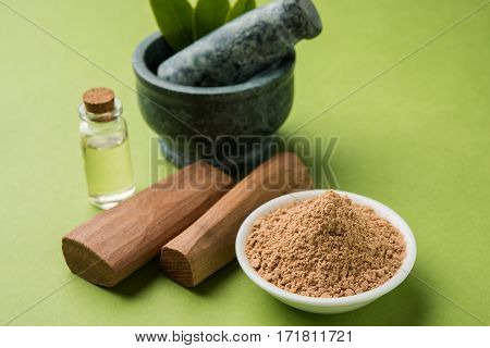 Chandan or sandalwood powder with traditional mortar, sandalwood sticks, perfume or oil and green leaves. selective focus