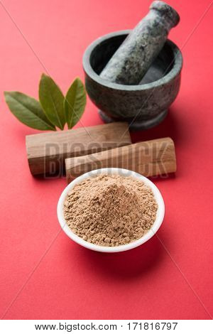 Chandan or sandalwood powder with traditional mortar, sandalwood sticks, perfume or oil and green leaves. selective focus
