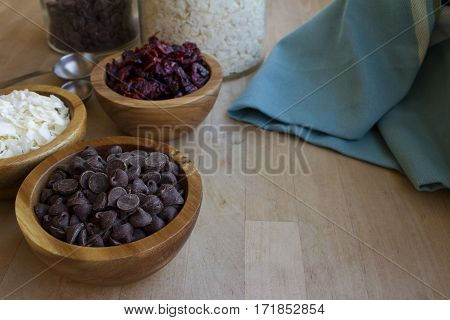 Wooden bowls filled with dried coconut shavings cranberries and chocolate chips.