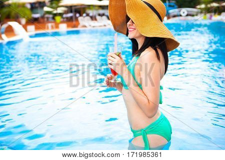 Beautiful Brunette Woman Wearing A Hat And Sunglasses, Enjoying Cocktail In A Swimming Pool, Summer