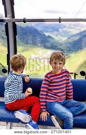 Two Little Boys Sitting Inside Of Cabin Of Cable Car And Looking On Mountains Landscape. Family On H