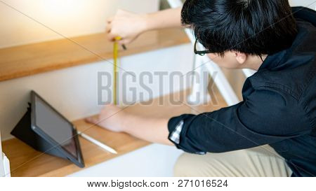 Young Asian Worker Using Tape Measure For Measuring Riser And Thread On Stair In The House. Writing 