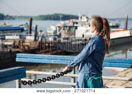 Fun Teenage Girl In Blue Denim Dress Is Walking In River Station. Young Cheerful Child Piddle In Riv
