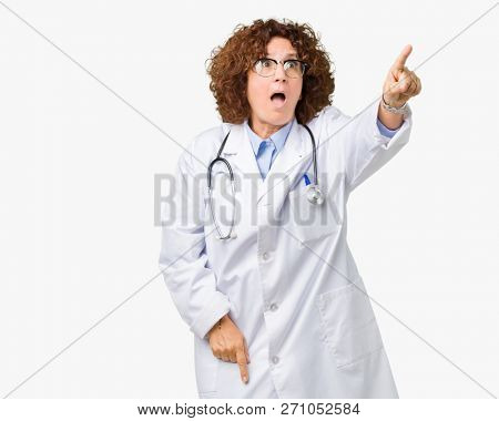 Middle ager senior doctor woman over isolated background Pointing with finger surprised ahead, open mouth amazed expression, something in front