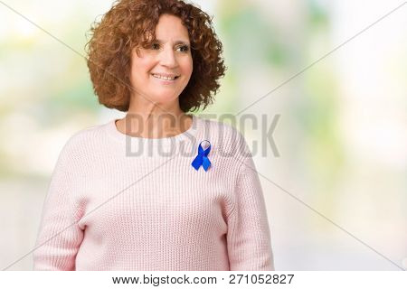 Middle ager senior woman wearing changeable blue color ribbon awareness over isolated background looking away to side with smile on face, natural expression. Laughing confident.