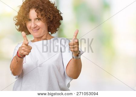 Beautiful middle ager senior woman wearing white t-shirt over isolated background pointing fingers to camera with happy and funny face. Good energy and vibes.