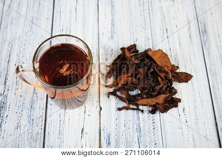 Cup Of Hot Black Tea And Dried Tea Leaves On Wooden Table Top View