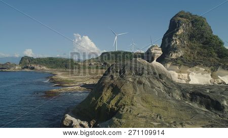 Natural Rock Formation Of Limestone Stone On The Coast With Windmills For Electric Power Production.