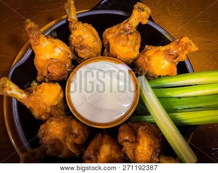 Delicoius Chicken Wings And Celery Sticks Placed In A Round Plate With A Small Bow Of White Sauce In