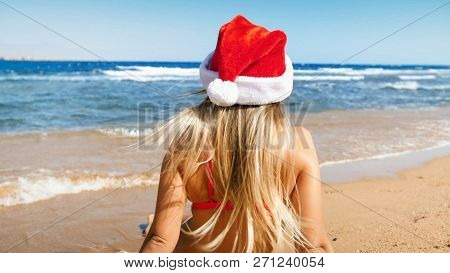 Rear View Image Of Young Woman In Long Hair Wearing Santa Clauss Hat Looking At The Sea. Concept Of 