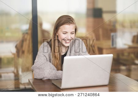 Portrait Of Young Attractive Woman At Office Desk, With Laptop, The Girl Smiles At The Computer Happ
