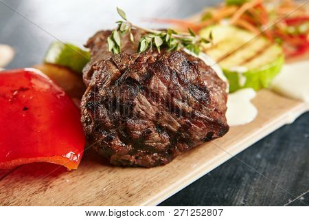 Hot Grilled Beef Tenderloin Steak, Barbecue Sirloin Meat on Wooden Background with Bbq Vegetables. Macro Photo of Fresh Juicy Deep Fried Veal Grillsteak Close Up
