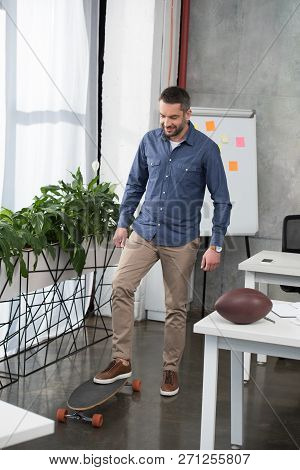 Cheerful Handsome Businessman Putting Leg On Longboard In Office